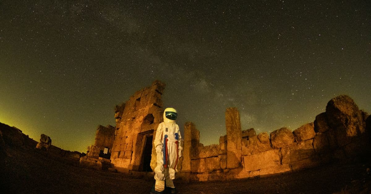 A spacesuit-clad figure stands against the backdrop of ancient Diyarbakır ruins under a starry night sky.
