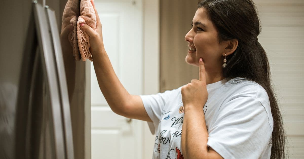 A woman cheerfully wipes a refrigerator, showcasing a moment of home cleaning.