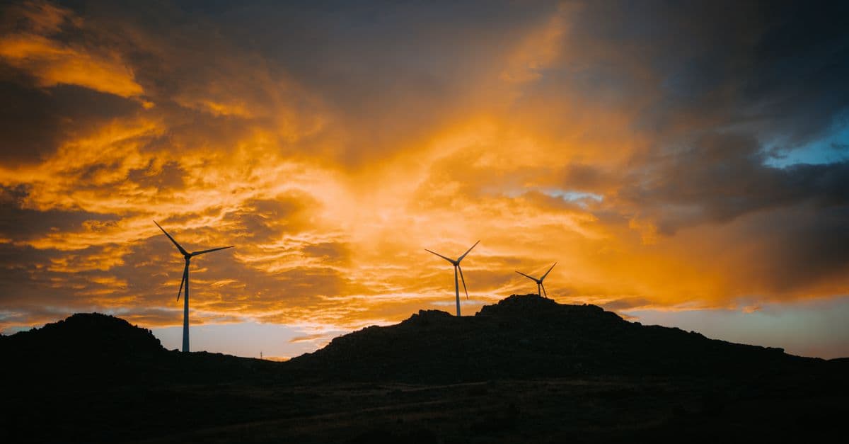 Three wind turbines silhouetted on a hill at sunset, showcasing renewable energy on a dramatic landscape.