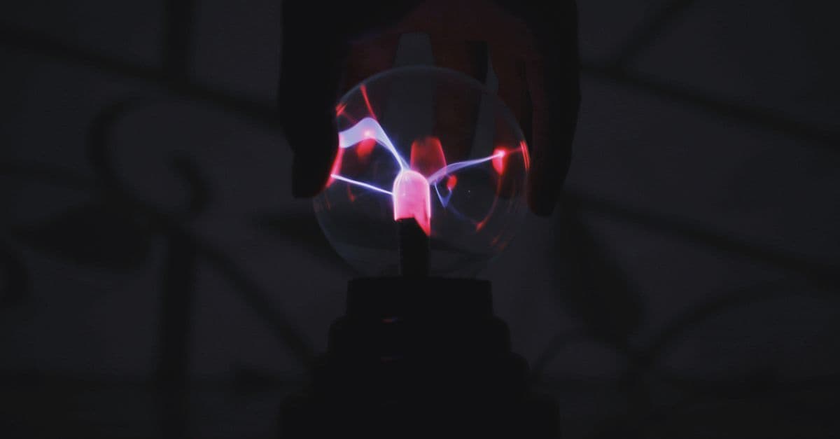 Crop anonymous person touching plasma ball with magic colorful light in dark room