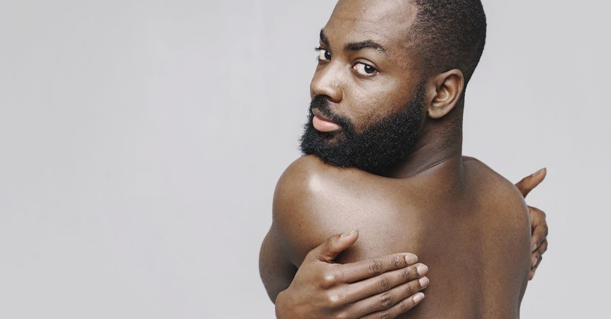 Shirtless man with beard and shaved head posing against a white background.
