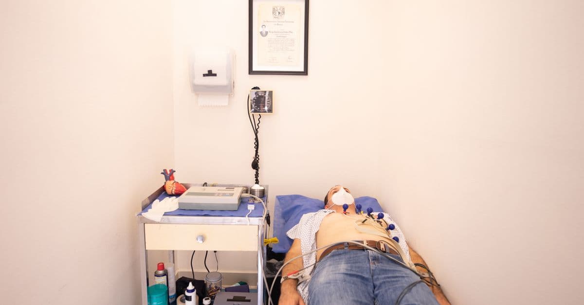 Patient lying down for an electrocardiogram in a clinic room wearing a face mask.