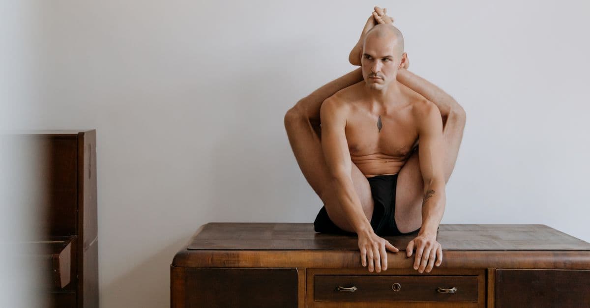 Bald acrobat performing a contortion pose on a wooden desk, showcasing extreme flexibility.