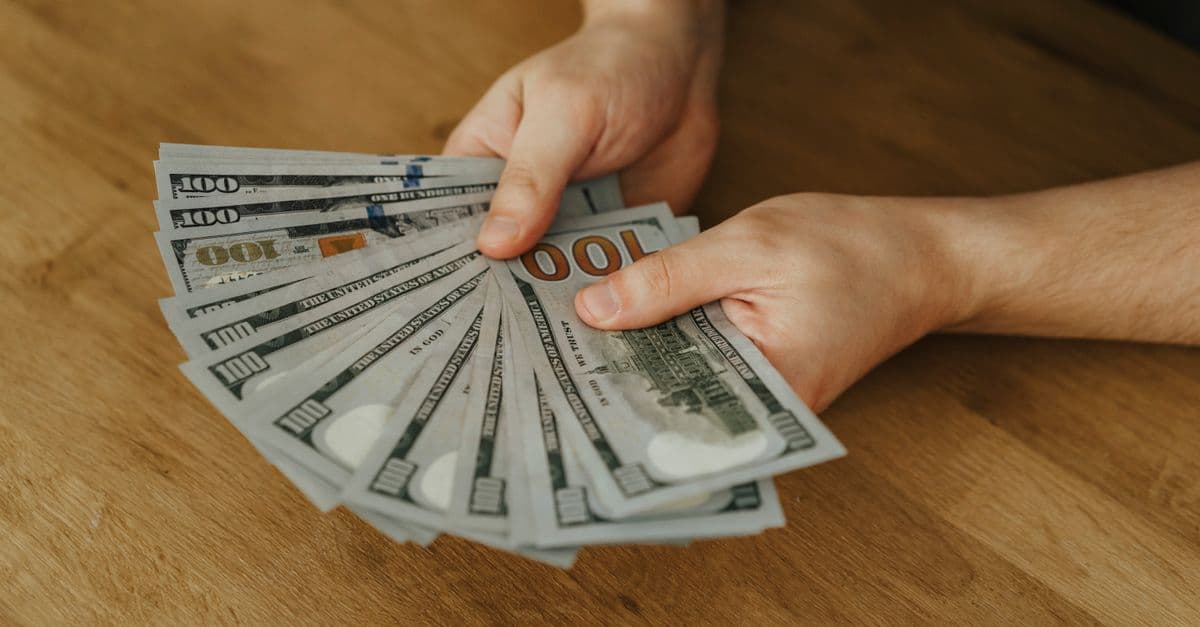 Close-up of hands holding several 100 US dollar bills on a wooden surface.