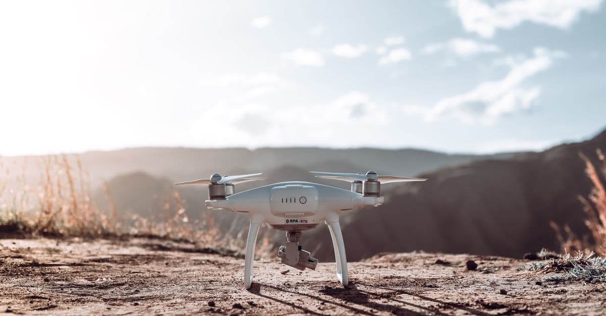 A white drone rests on a mountain terrain under a clear sky, ready for flight.