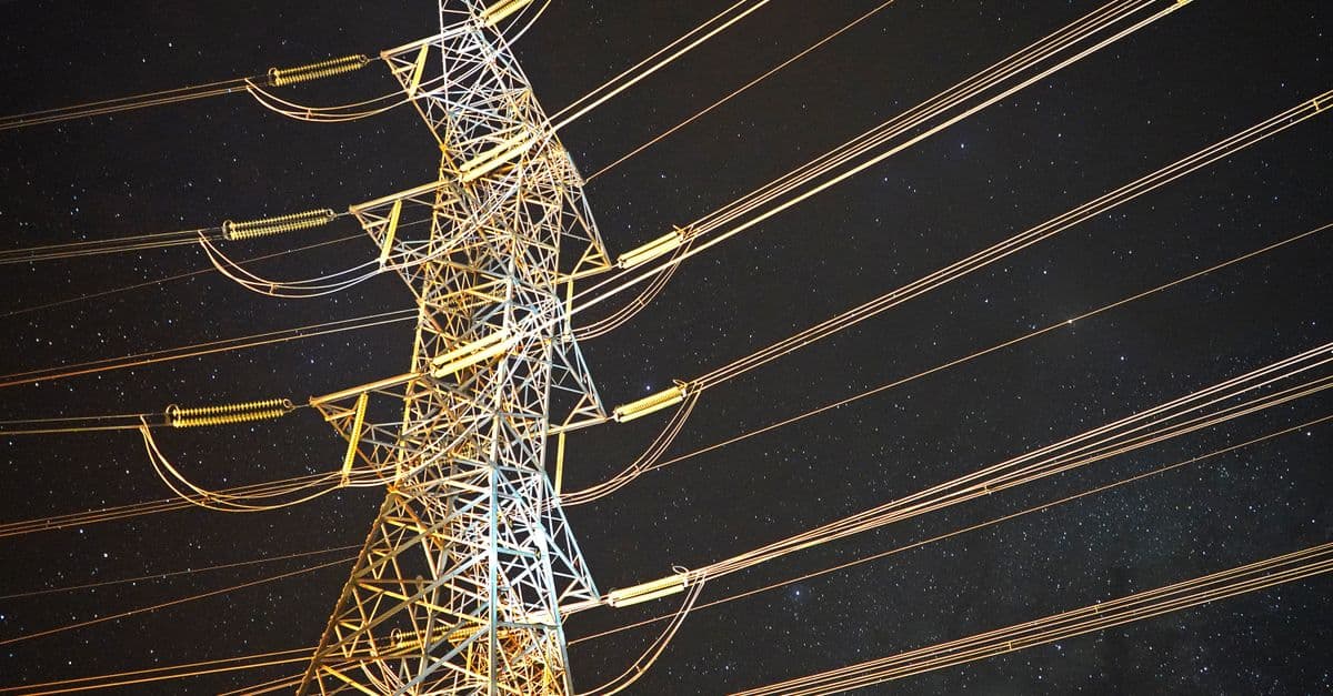 Illuminated power tower against a starry night sky, showcasing energy infrastructure.