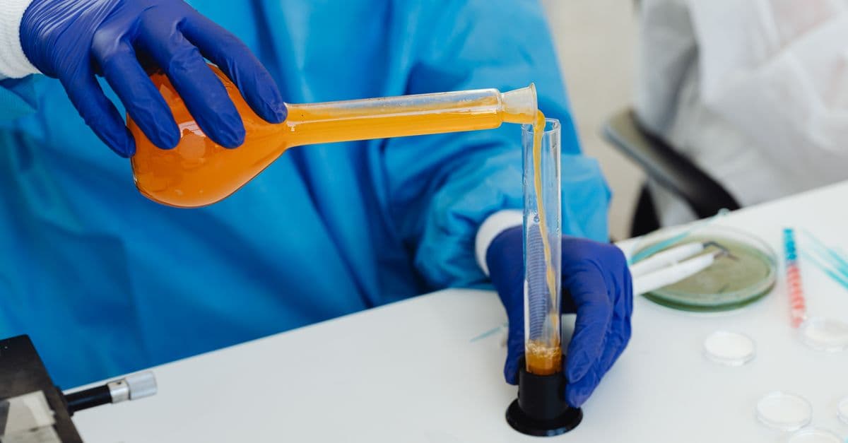Close-up of a scientist pouring orange liquid into a vial in a laboratory setting.