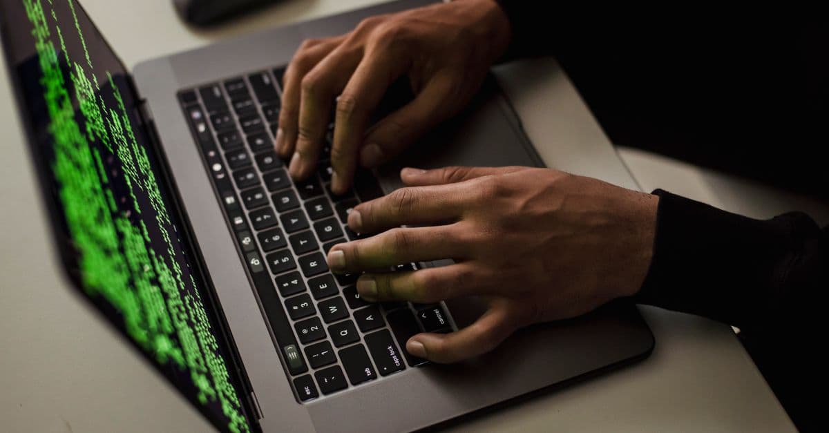From above of crop anonymous male hacker typing on netbook with data on screen while sitting at desk