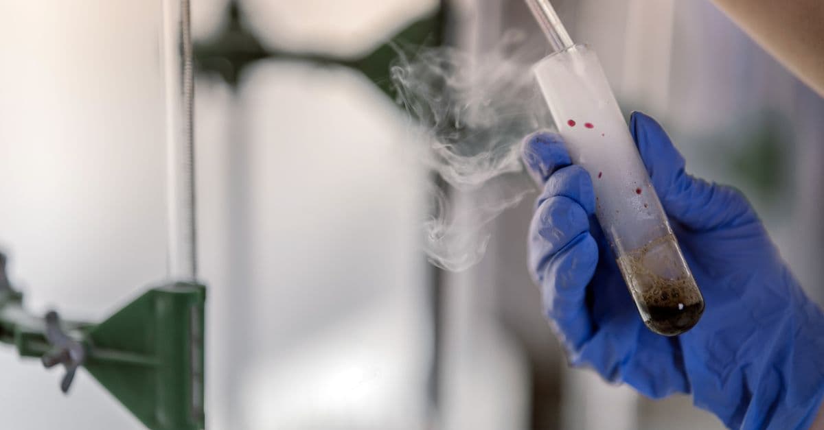 Close-up of a gloved hand holding a steaming test tube in a laboratory setting.