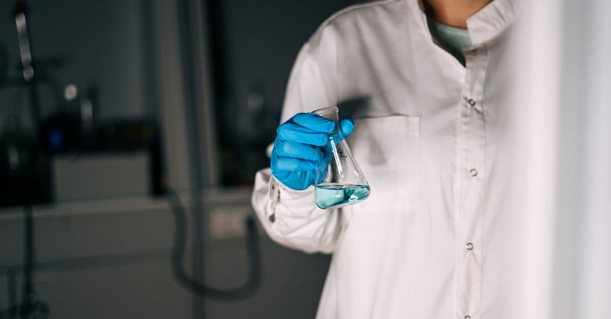 Scientist in white coat holding a flask with blue liquid in a laboratory, showcasing scientific research.