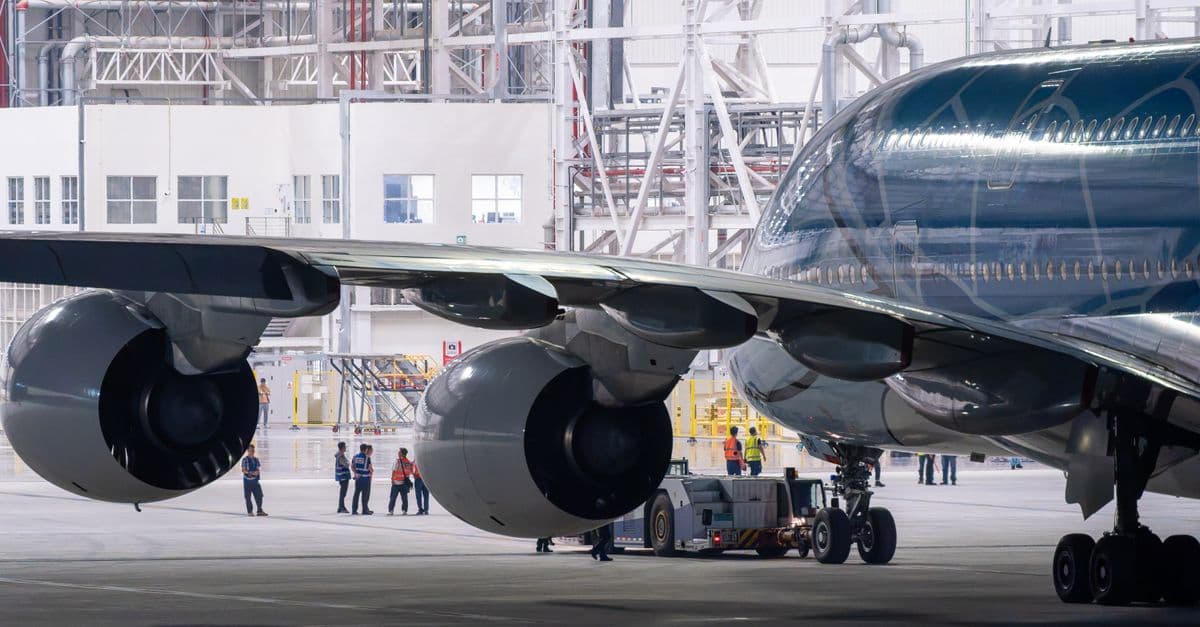Close-up of an airplane's engines and fuselage inside a maintenance hangar, featuring crew staff.