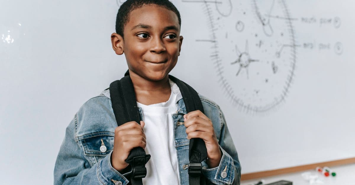 Happy African American boy with backpack near modern whiteboard with structure of primitive organism