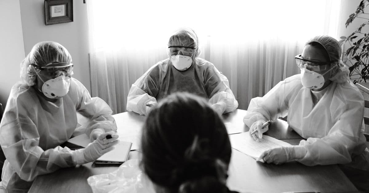 Black and white photo of healthcare team in PPE holding a meeting indoors.