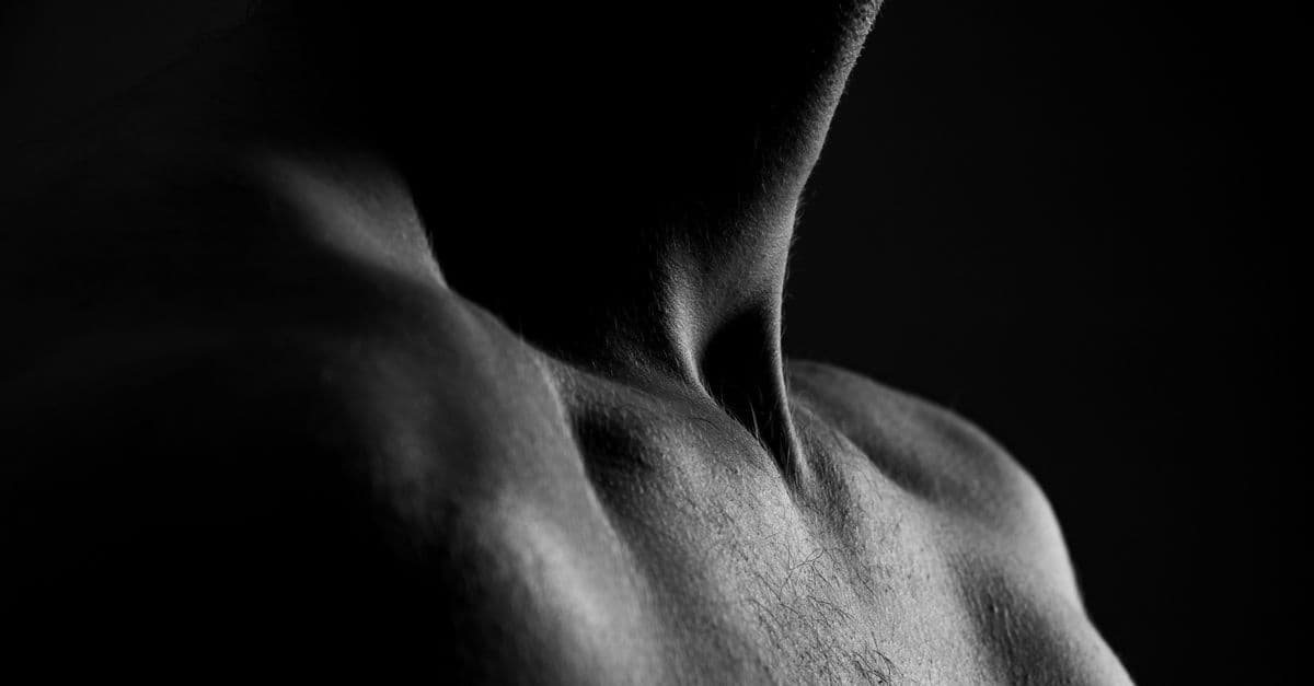 Dramatic grayscale close-up of a male torso showcasing strong light and shadow contrast.