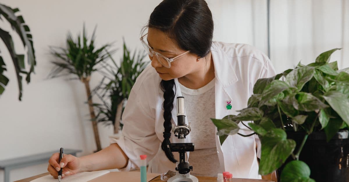 Female scientist conducting research and taking notes with microscope and plants.