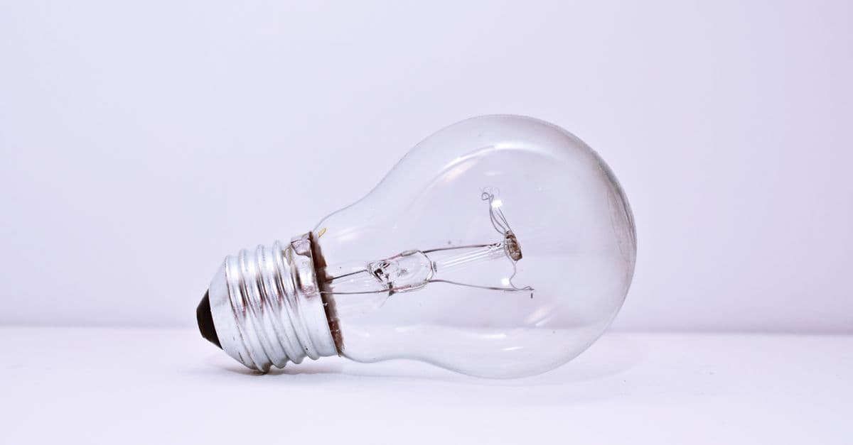 A clear incandescent light bulb lying on a simple white background, showcasing minimalism.