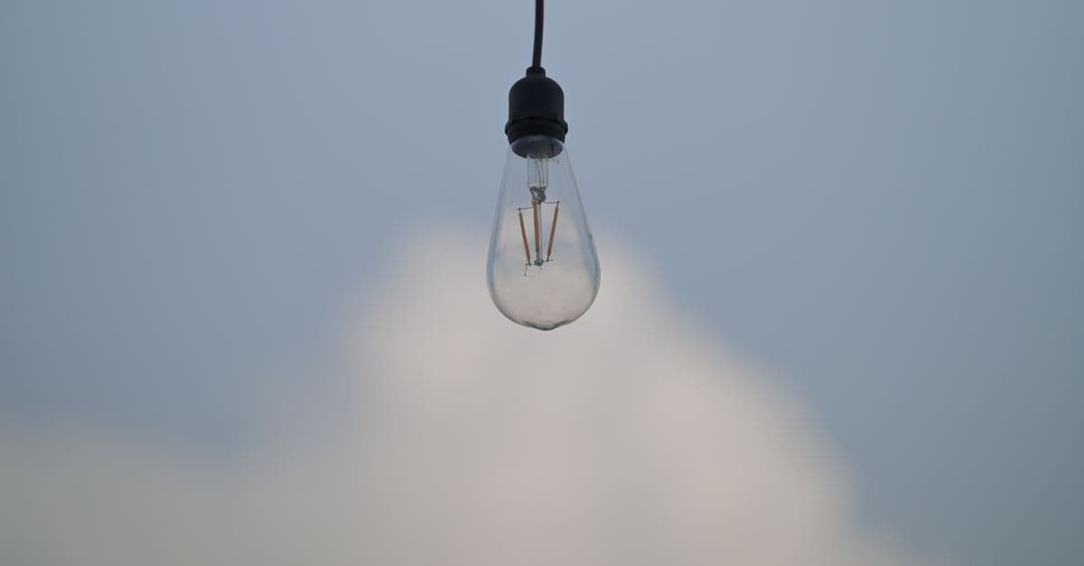 A single light bulb suspended against a soft blue sky, evoking simplicity and innovation.