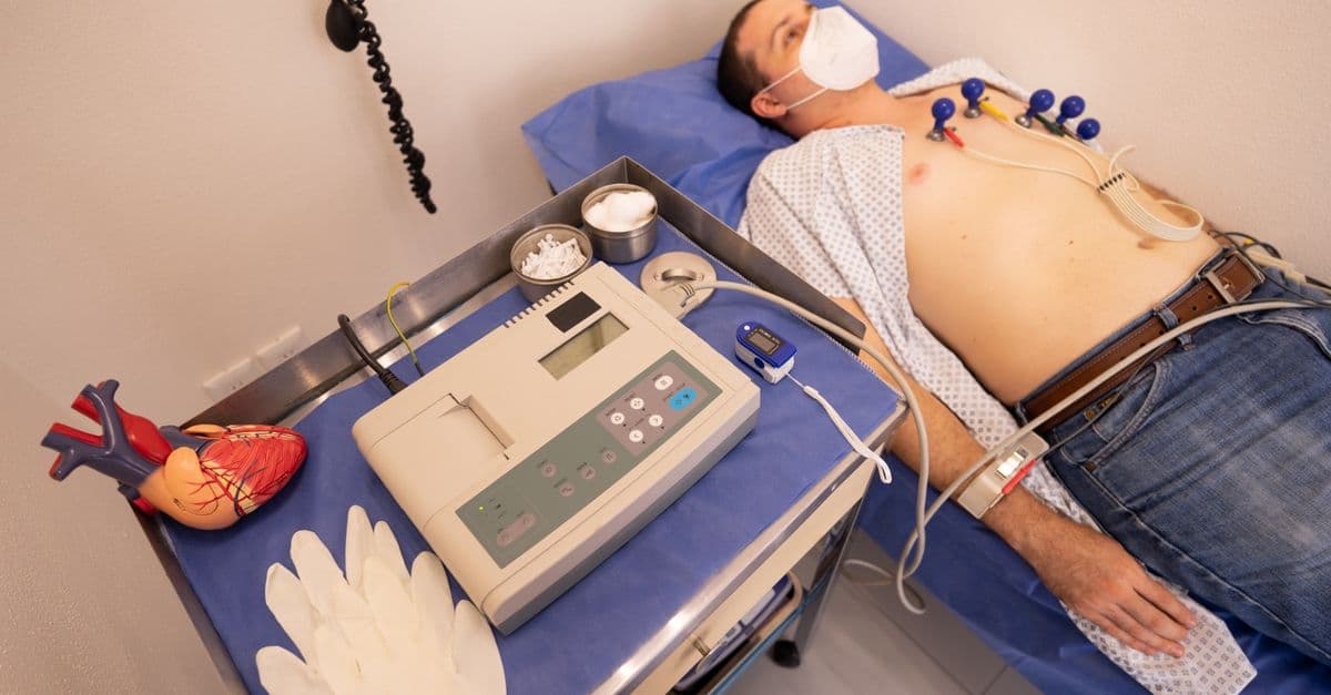 A man undergoing a cardiology exam with an ECG machine in a medical clinic.