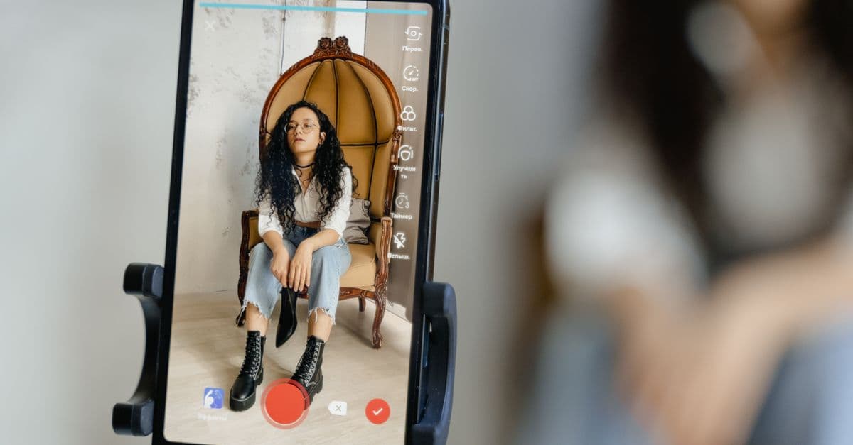 A woman sits in a chair recording a video on her smartphone, showcasing modern vlogging techniques.