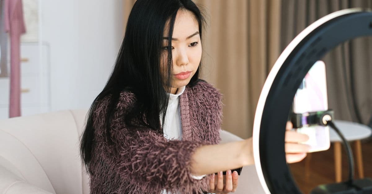 An Asian woman vlogs at home using a smartphone and ring light, perfect setup for influencers.