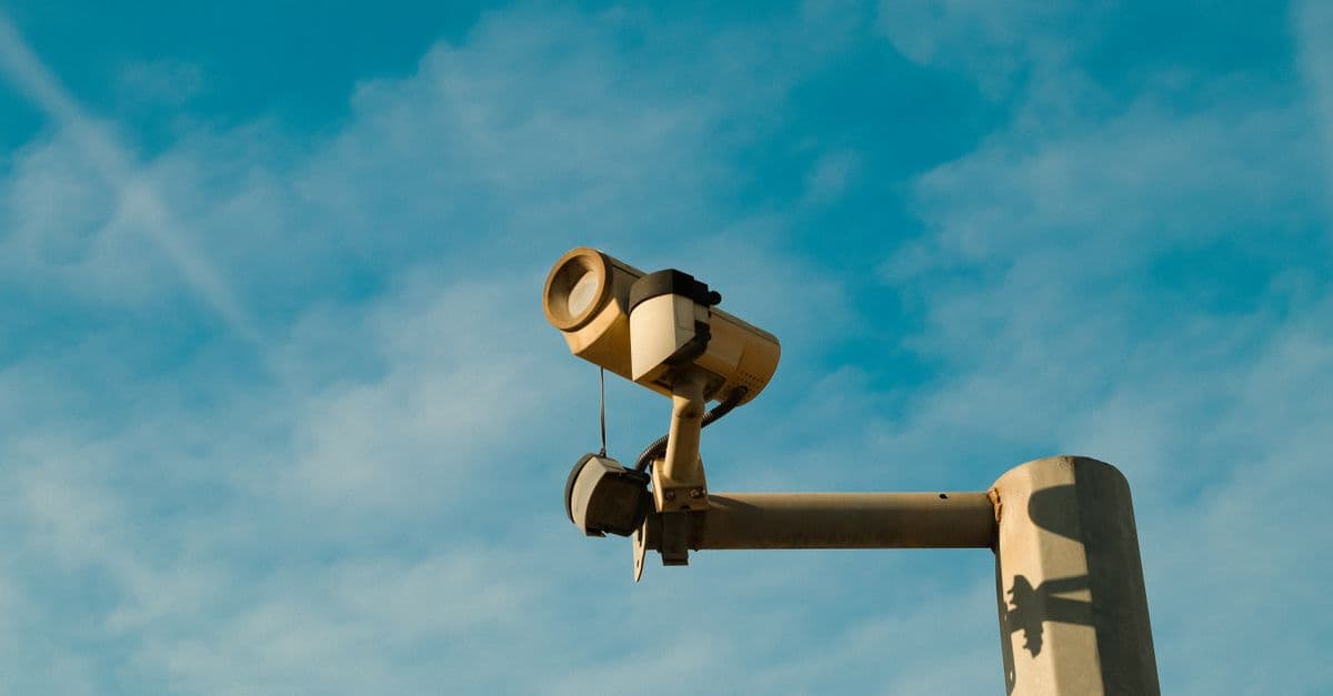 A surveillance camera mounted outdoors against a bright blue sky, symbolizing security and monitoring.