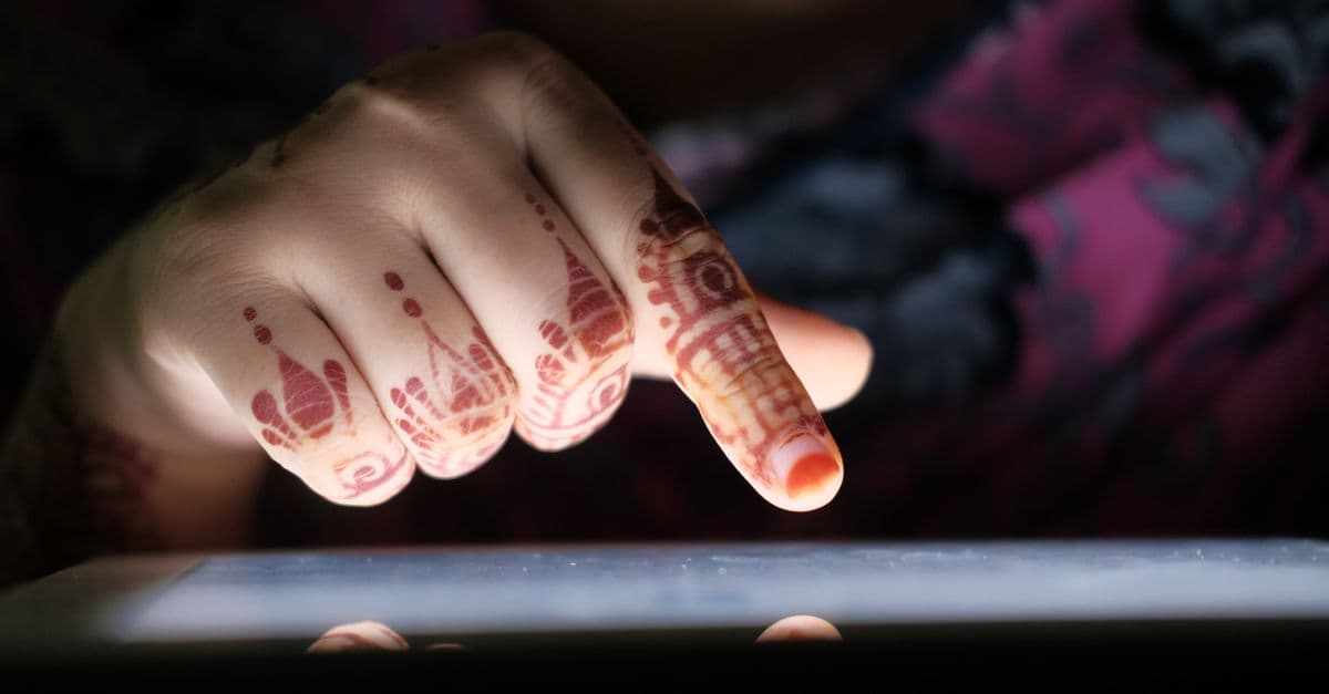 Intricate mehndi design on a woman's hand interacting with a digital tablet.
