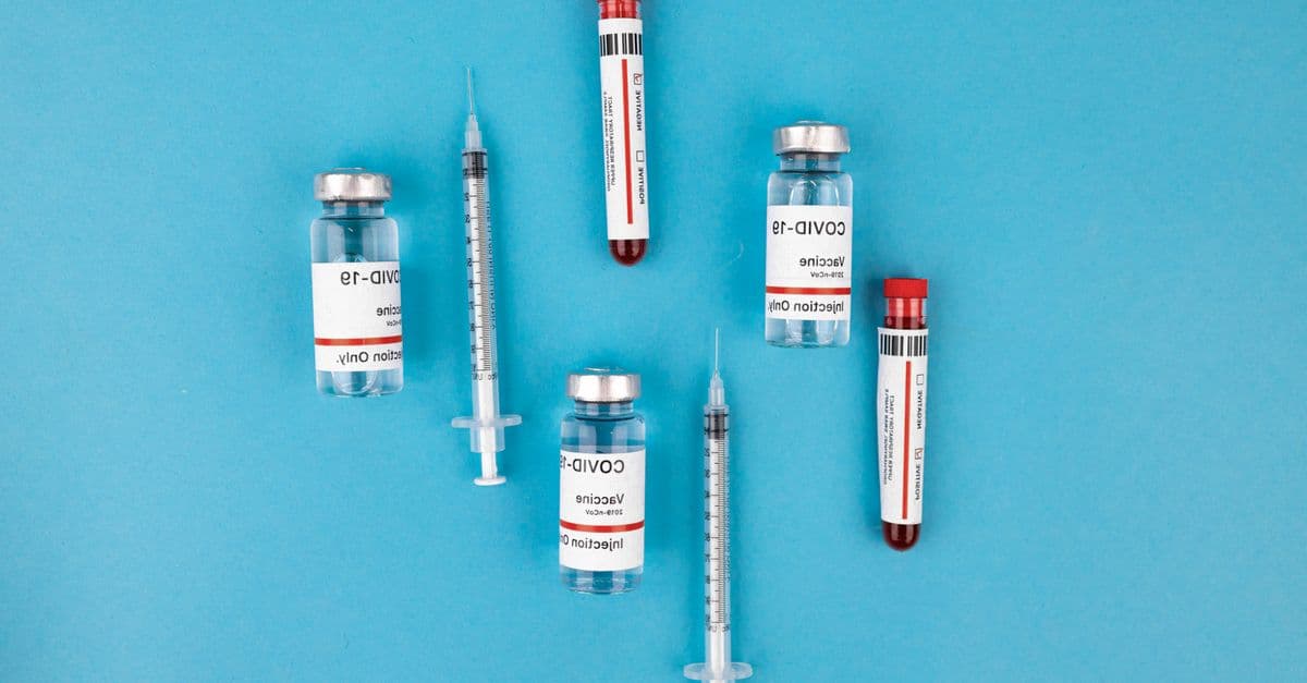Top view of COVID-19 vaccine vials, syringes, and test tubes on a blue background, representing immunization and protection.