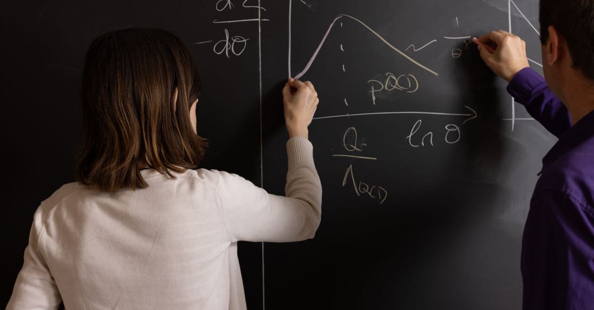 Teachers collaborating on mathematical equations and graphs on a chalkboard in an educational setting.
