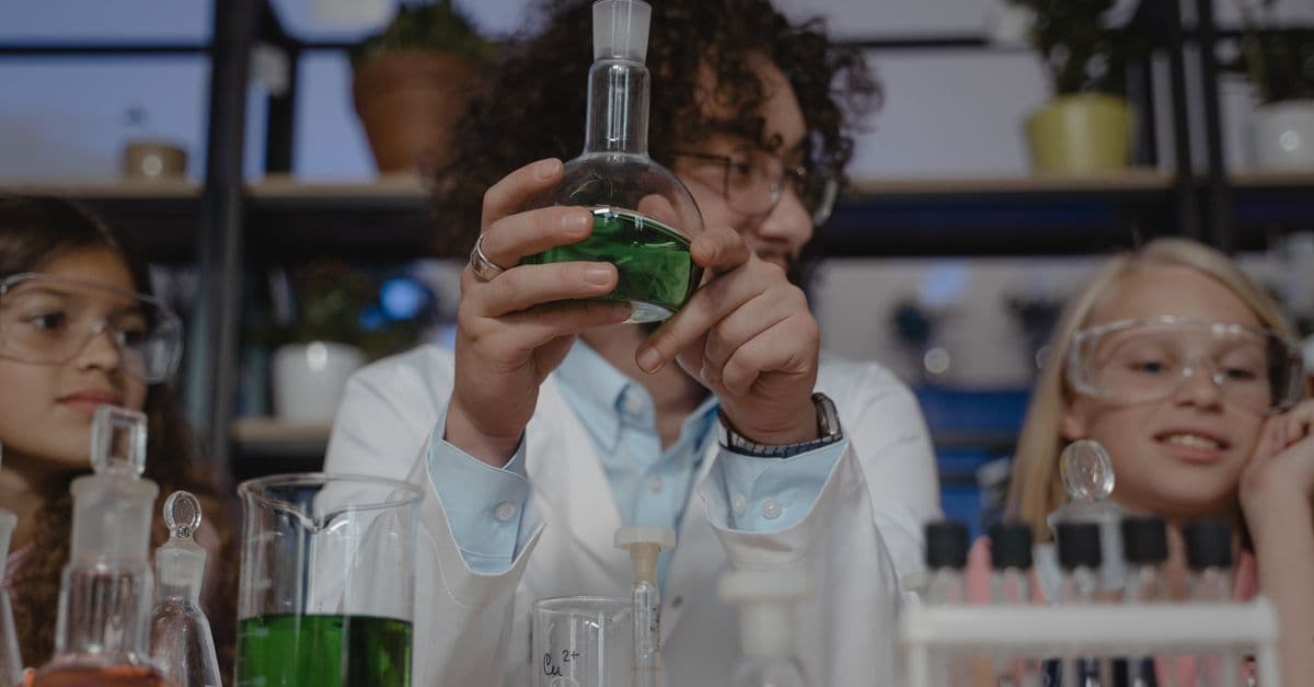 Students working on a chemistry experiment with flasks and colored liquids in a classroom setting.