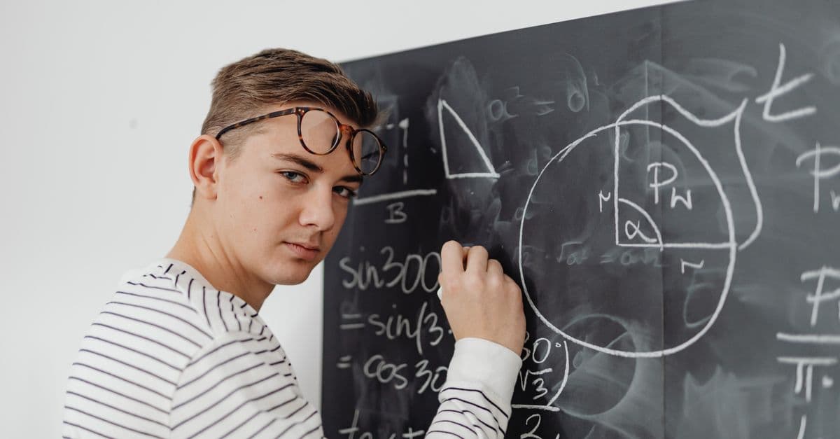 A teenager writes mathematical equations on a blackboard, focusing on geometry and trigonometry.