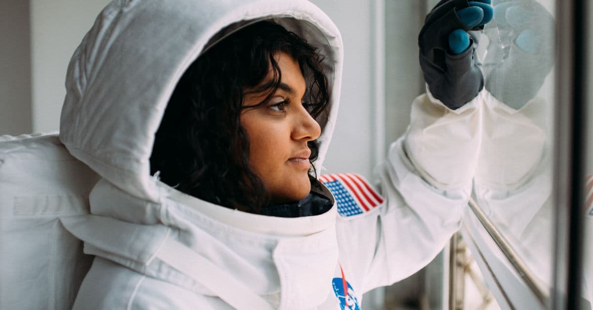 A woman in an astronaut suit looks thoughtfully out of a window, embodying space exploration dreams.
