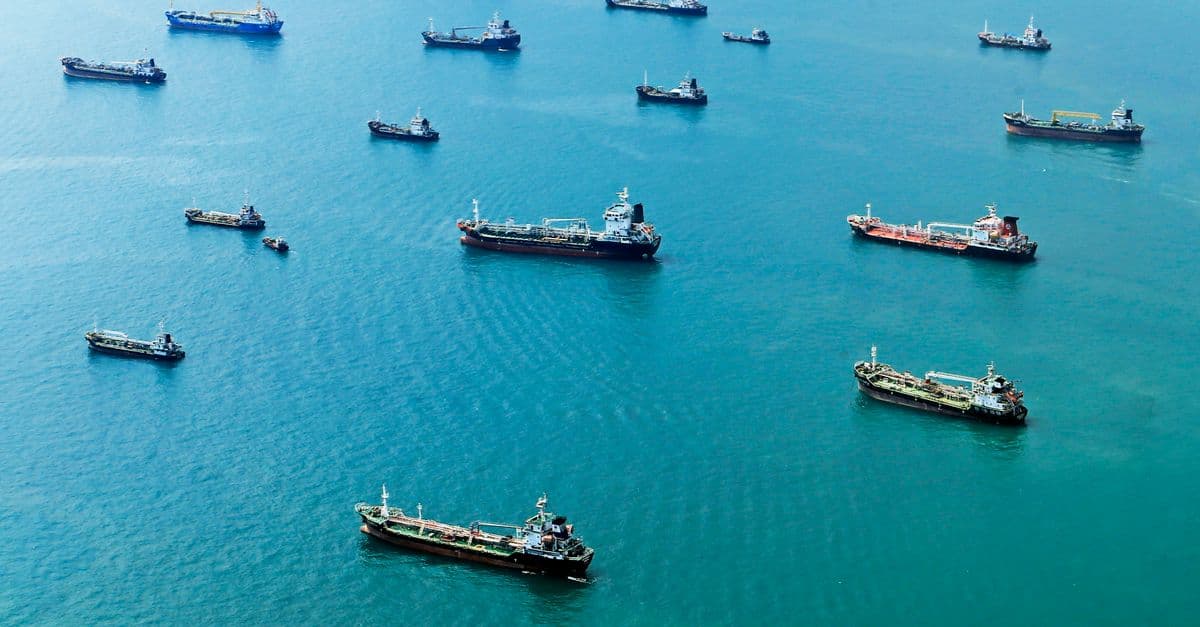 Numerous cargo ships anchored on the blue ocean, captured from above.
