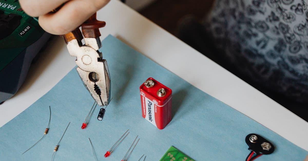 Close-up of electronics repair using pliers with resistors and battery.