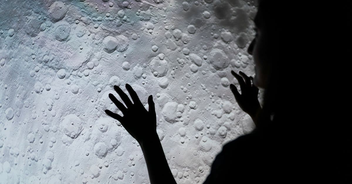 A mysterious silhouette of a woman interacting with a moon surface projection, evoking exploration and wonder.