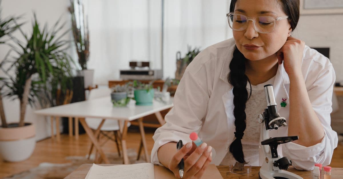 Female scientist in a lab coat working indoors with a microscope and notebook.