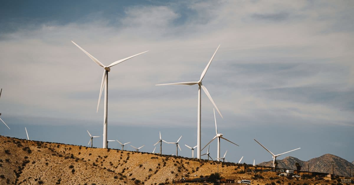 Wind turbines on a sunny desert hillside with clear skies, showcasing renewable energy use.