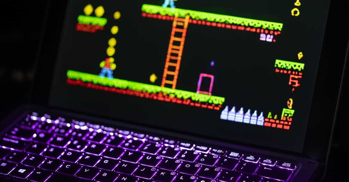 Close-up of a laptop displaying a retro video game with a neon-lit keyboard, capturing the nostalgic gaming experience.