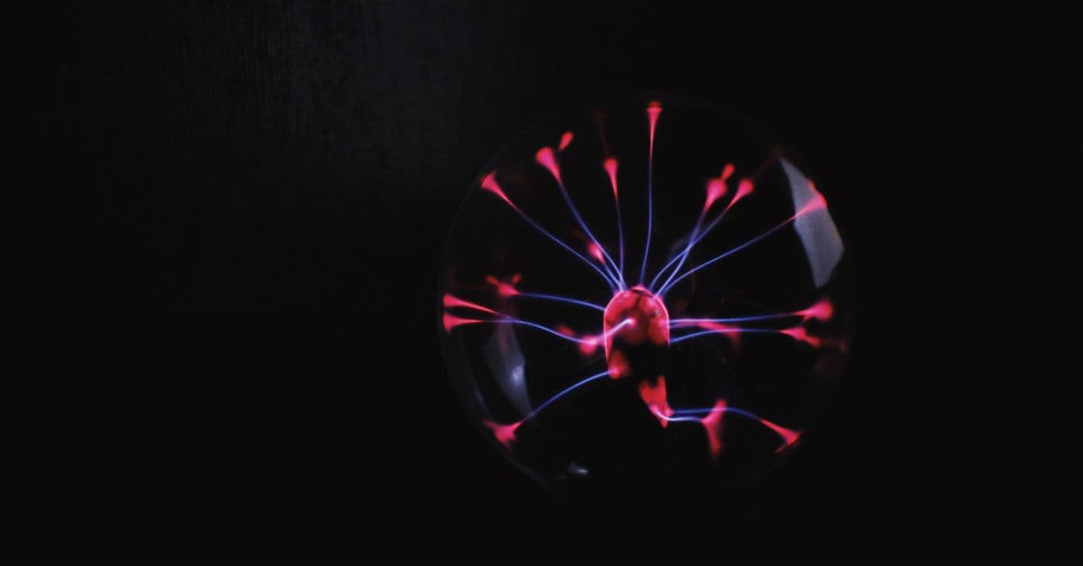 Round glass plasma ball with bright red electric lights placed in room against dark background