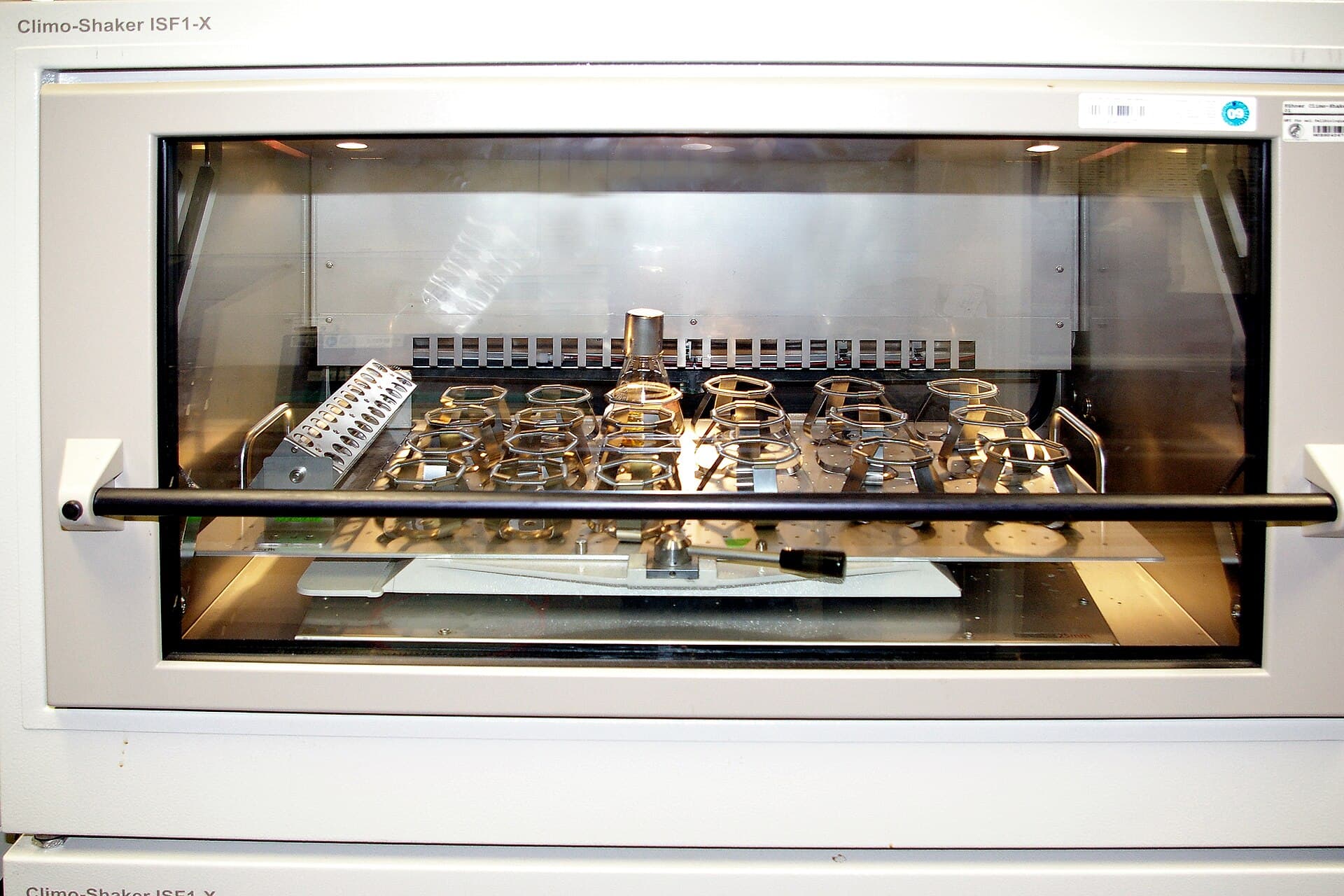 A laboratory shaker-incubator holding culture flasks, representing controlled three-dimensional cell culture research.