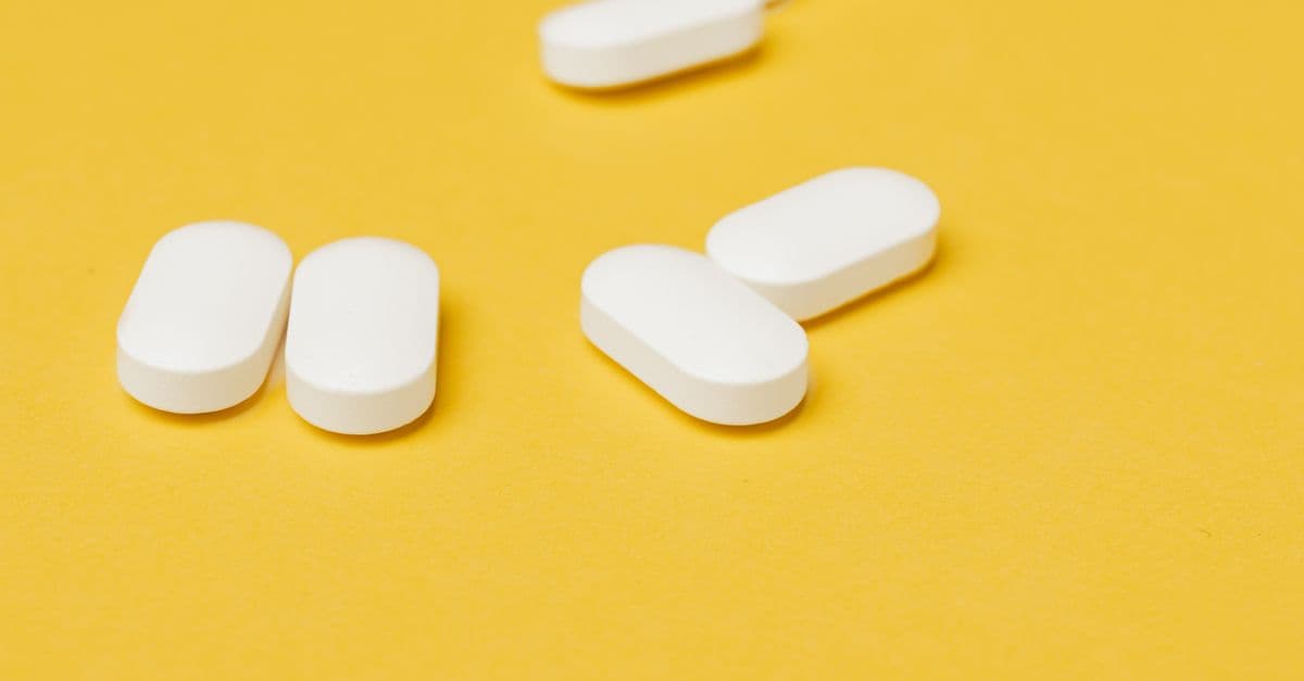 Set of medical white ellipse shaped pills placed in disorder on bright yellow background