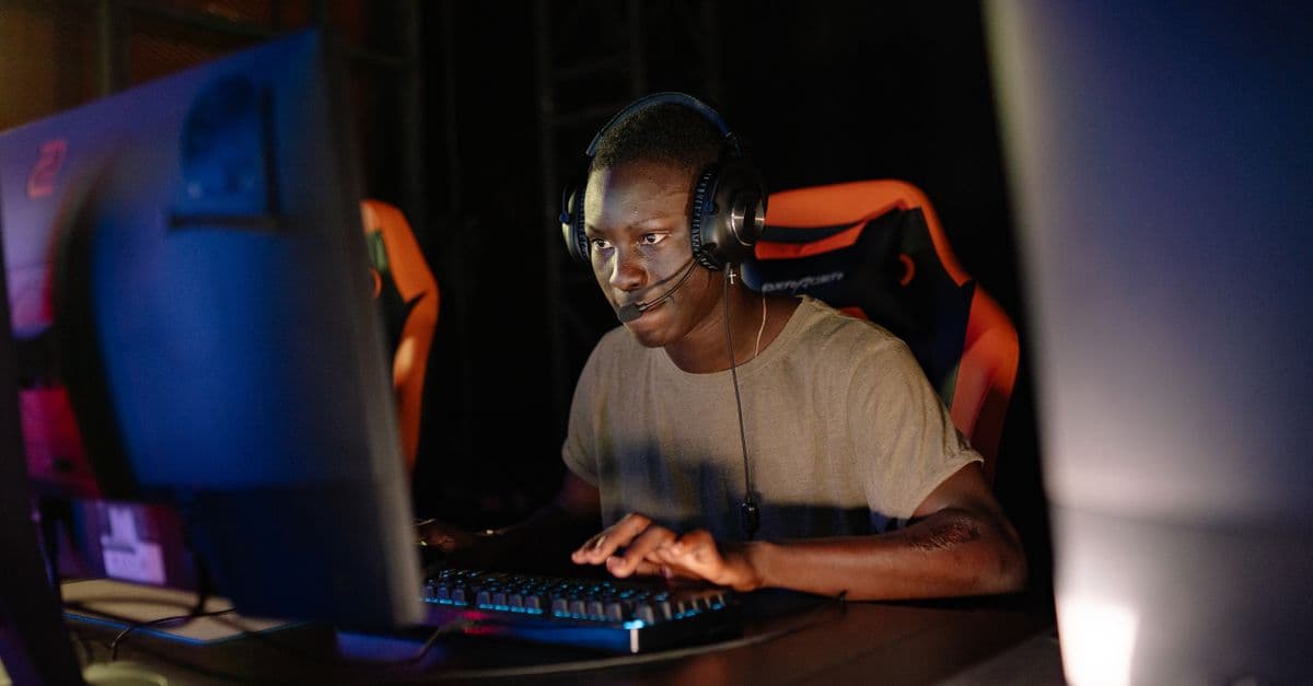 Young adult male intensely focused on computer gaming, using headset and gaming keyboard indoors.