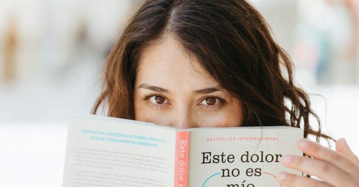 A woman reading a book titled 'Este dolor no es mío', focusing on mental health awareness.