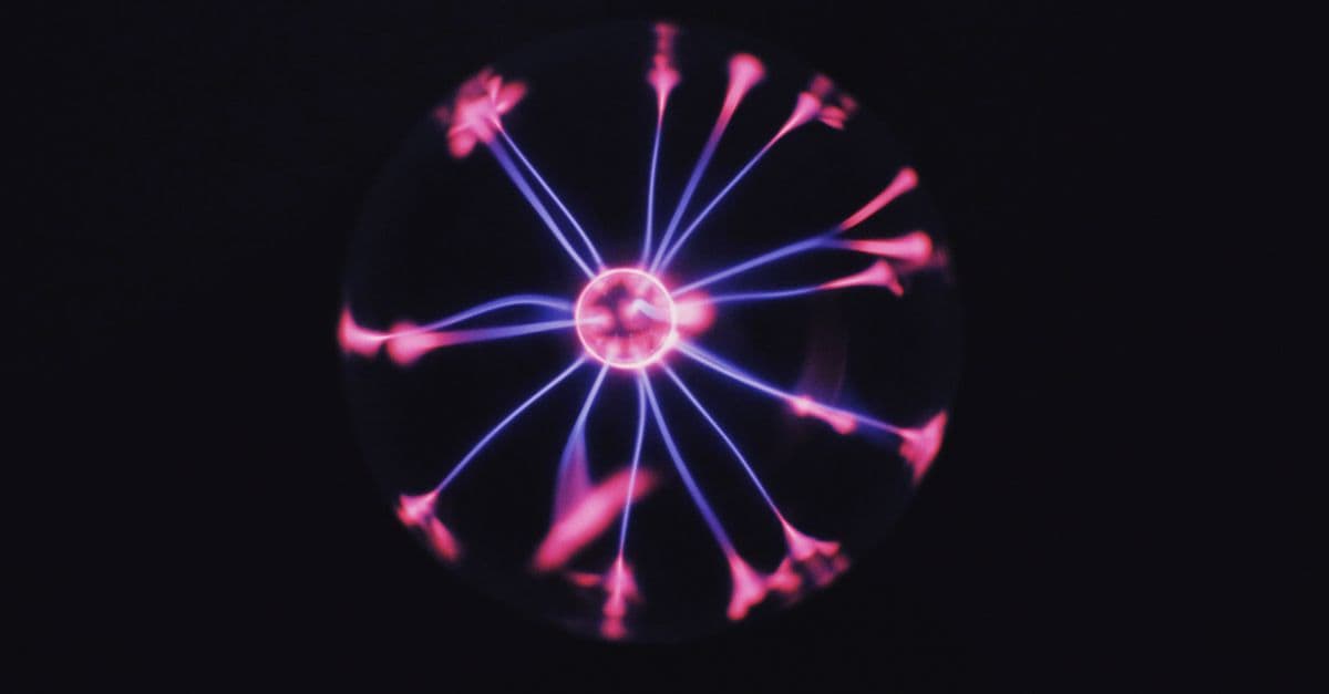 Transparent glass plasma ball with bright neon luminous against dark background in room
