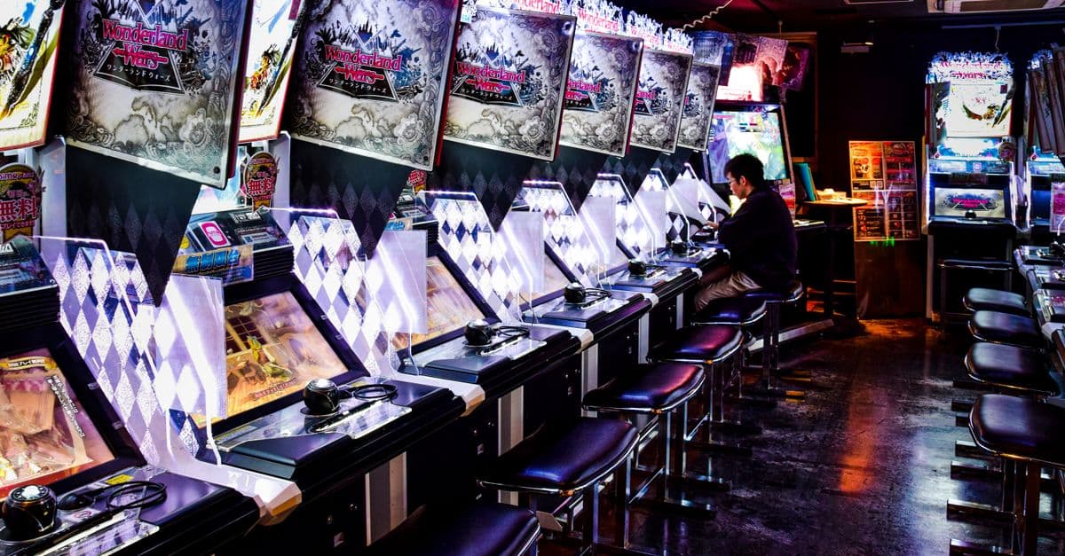 A man plays inside a modern arcade in Tokyo, illuminated by neon lights and gaming machines.