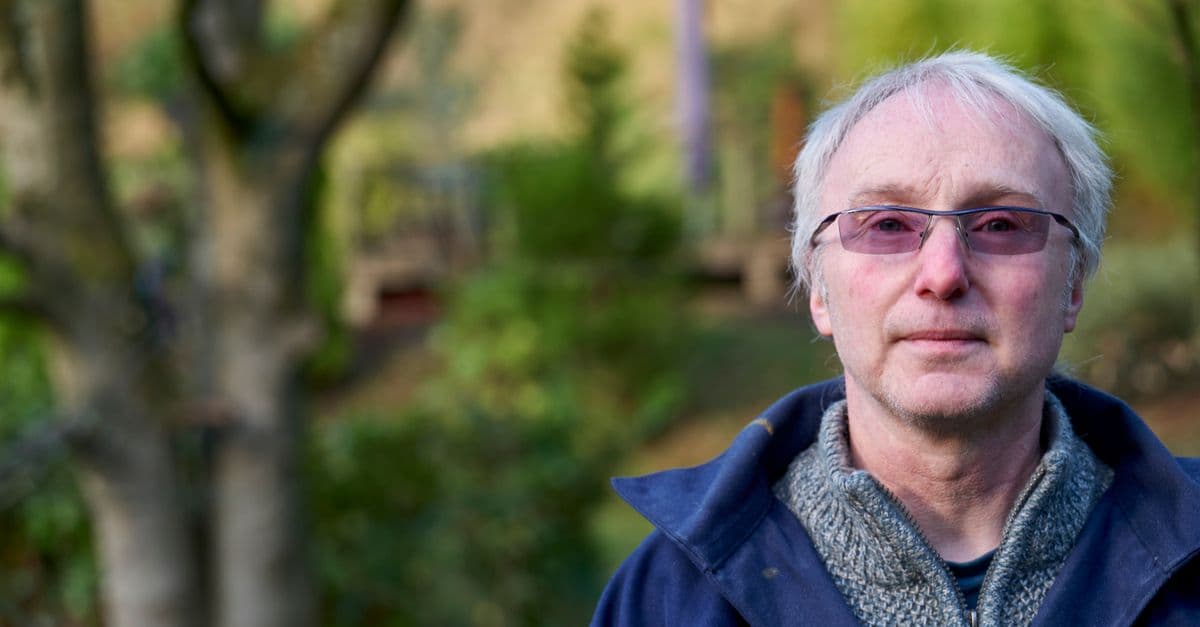 Senior Caucasian man with purple glasses outdoors, wearing blue jacket. Peaceful and thoughtful expression.