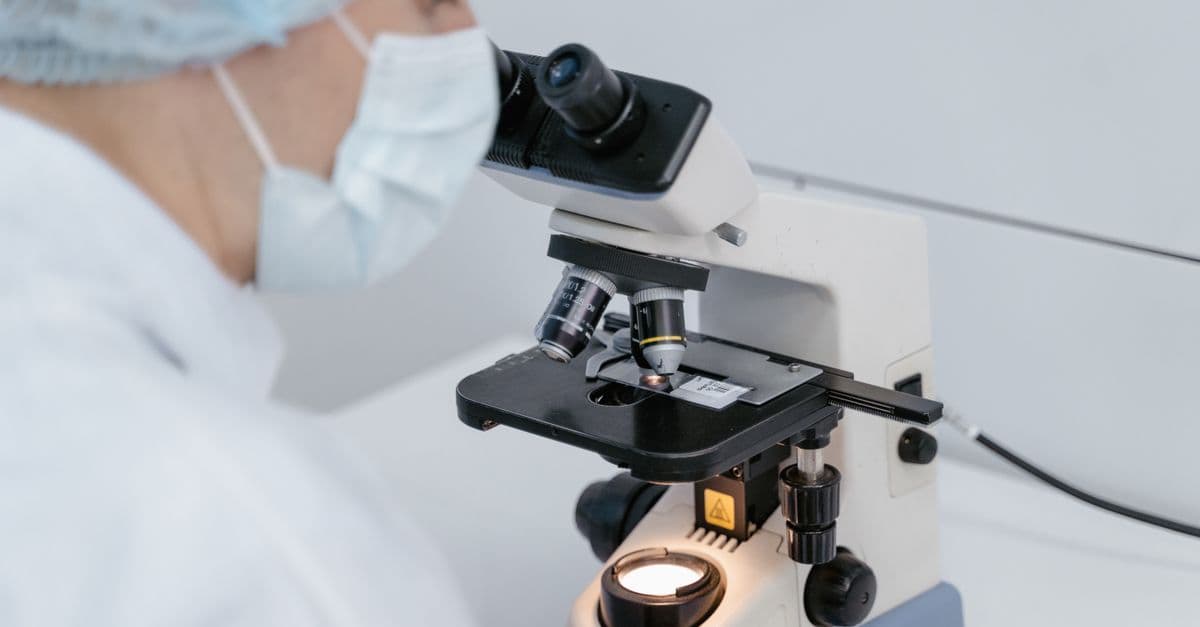 Scientist using a microscope in a laboratory setting, wearing protective gear.