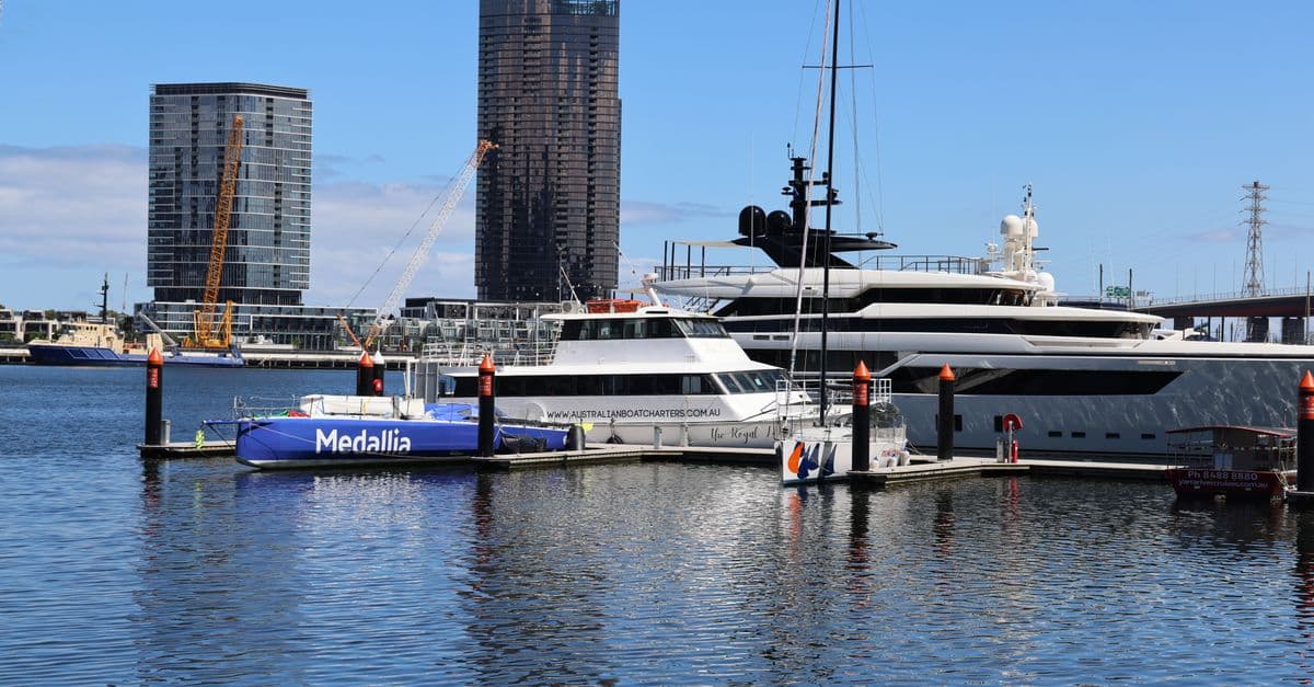 Luxury yachts docked at a marina with skyscrapers in the background under a clear sky.