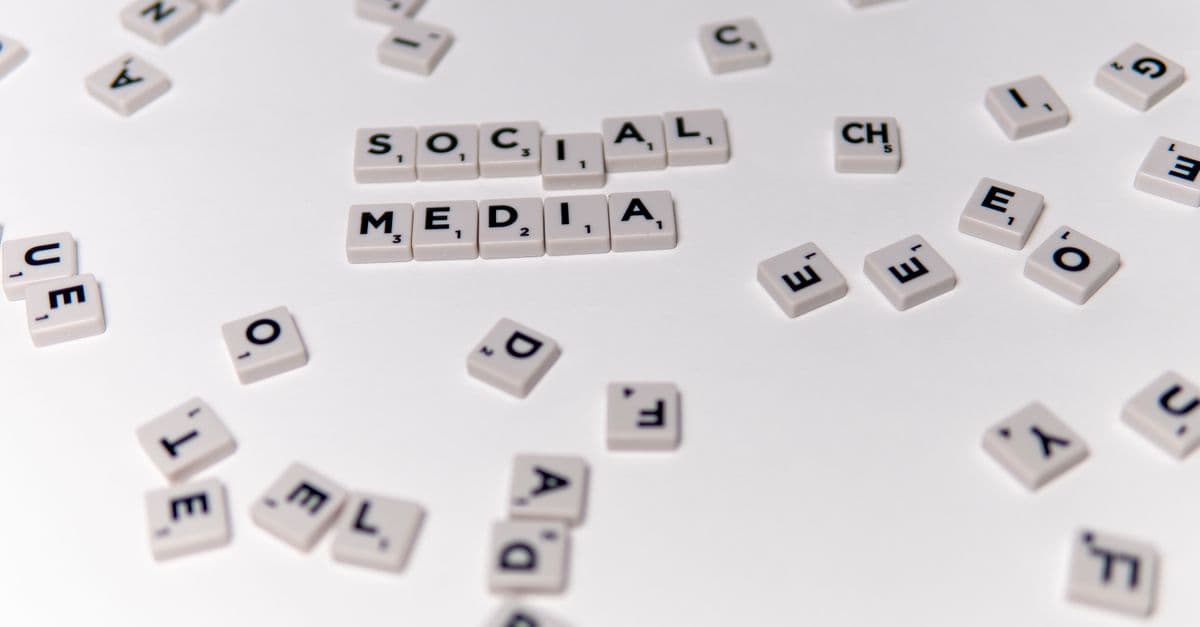 White Scrabble tiles forming the phrase 'social media' on a scattered background.