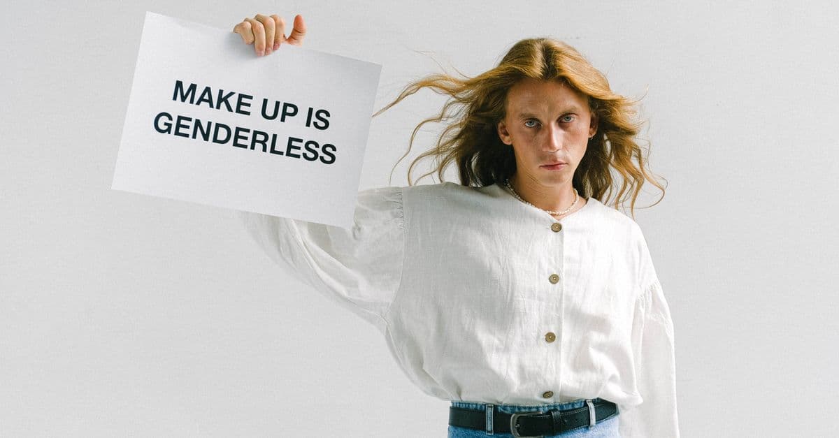 A person with long hair holds a sign stating 'Makeup is Genderless,' emphasizing inclusivity.
