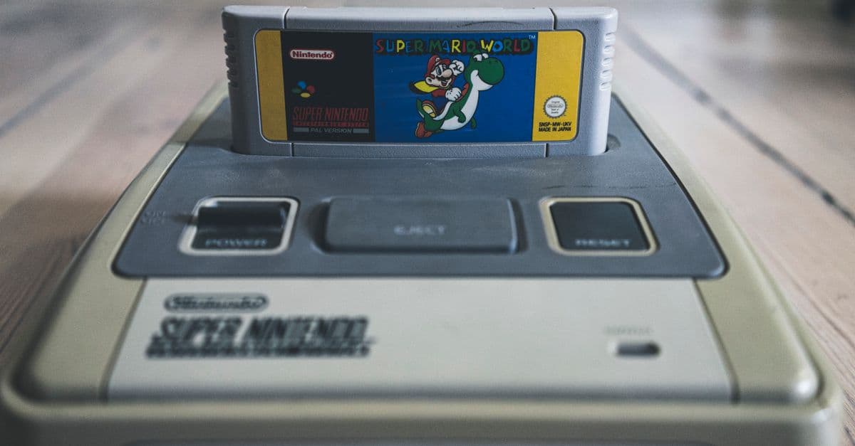 Vintage video game console with cassette with bright sticker on surface on wooden floor